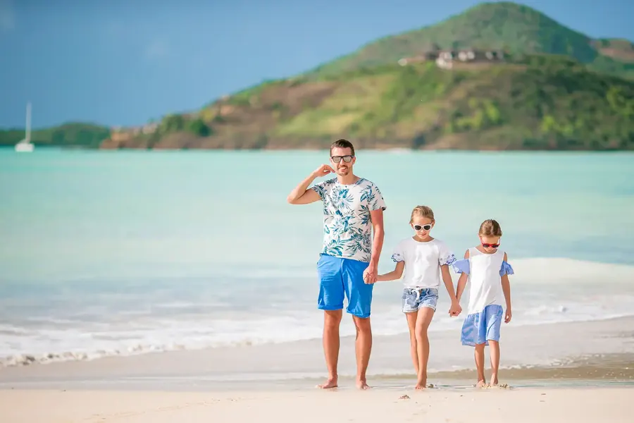 Father walking along a Mediterranean beach holding hands with his two daughters