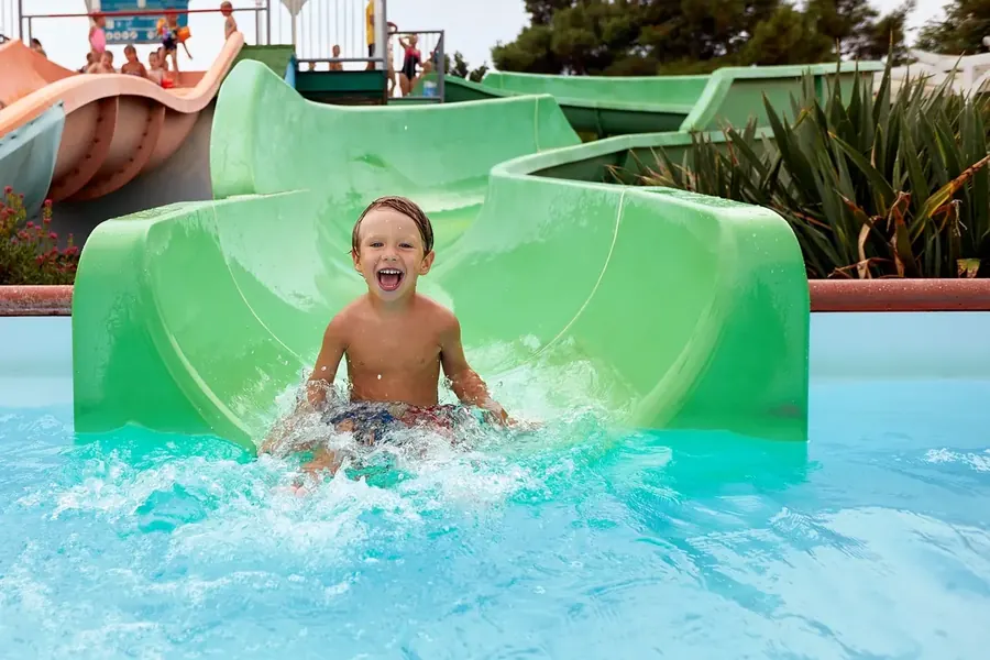 Boy laughing as he splashes down a green water slide