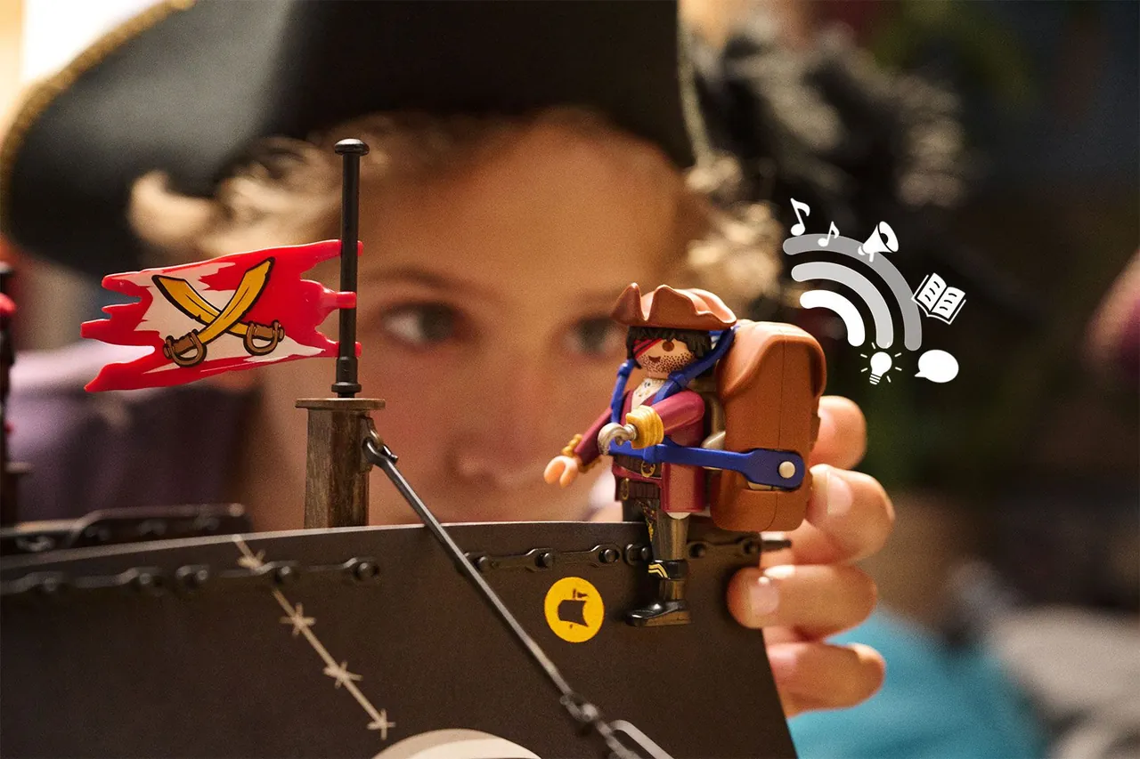 Child holding a Playmobil pirate figure wearing the Playmobil hi! audio backpack