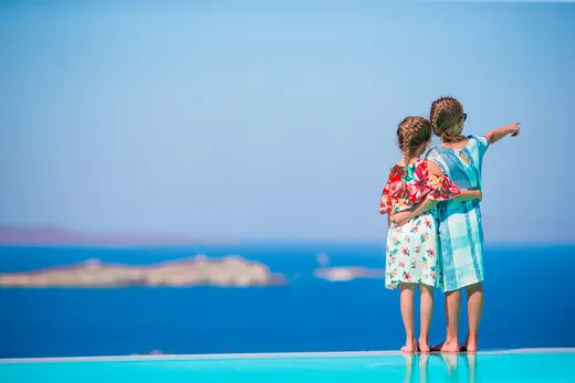 Two small girls standing at the edge of a pool looking at the sea